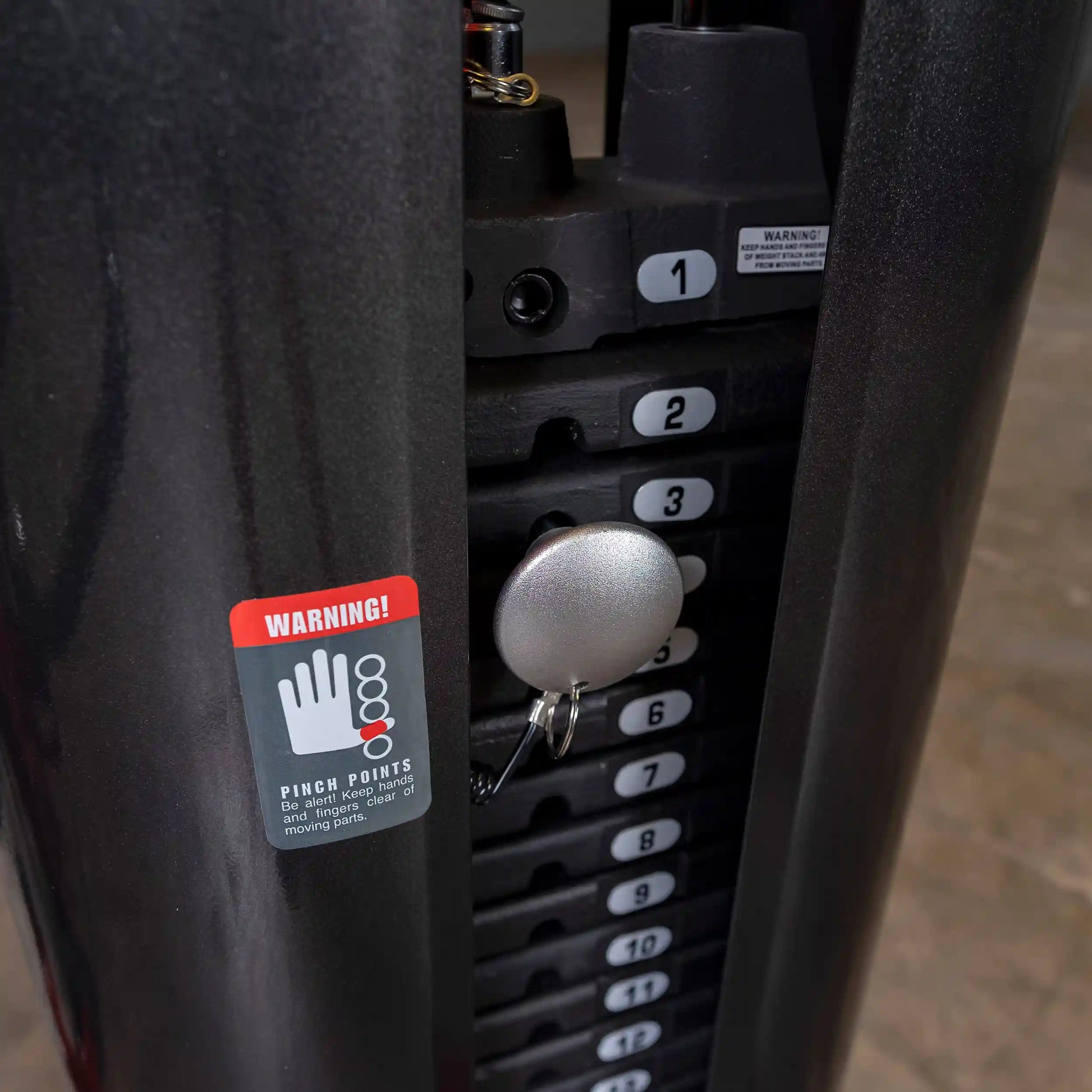 Gym weight stack with warning label and pin inserted for adjusting weights.