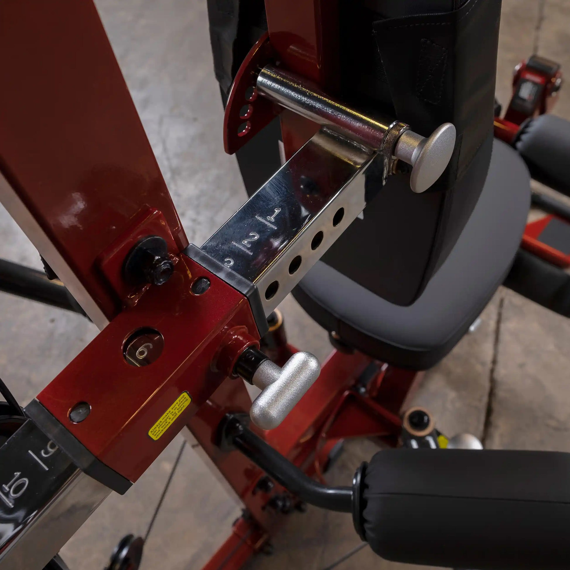 Red adjustable gym machine with chrome details and padded seat for strength training.