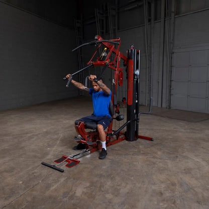 Man using Body-Solid home gym with red frame and pulldown bar in a spacious room.