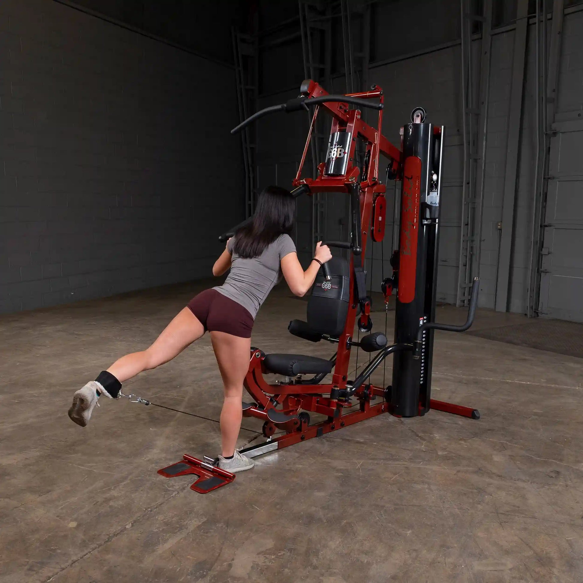 Woman using red Bowflex home gym for leg workout in industrial space.