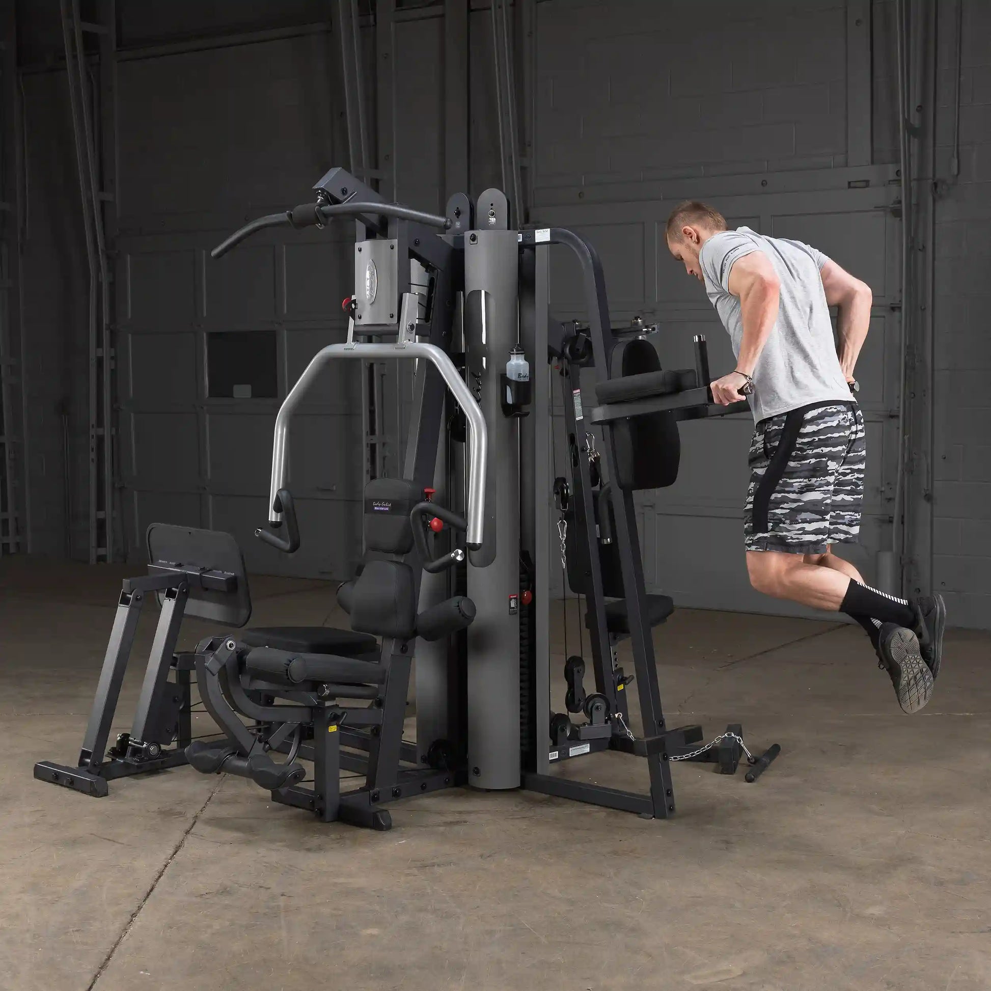 Man using Body-Solid home gym for tricep dips in a gray workout room.