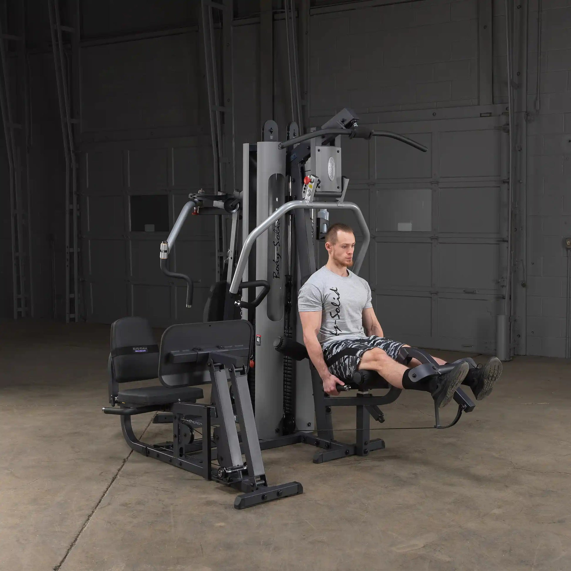 Man using Body-Solid home gym for leg exercise in a gray shirt and camo shorts.