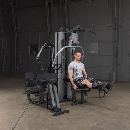 Man using Body-Solid home gym for leg exercise in a gray shirt and camo shorts.