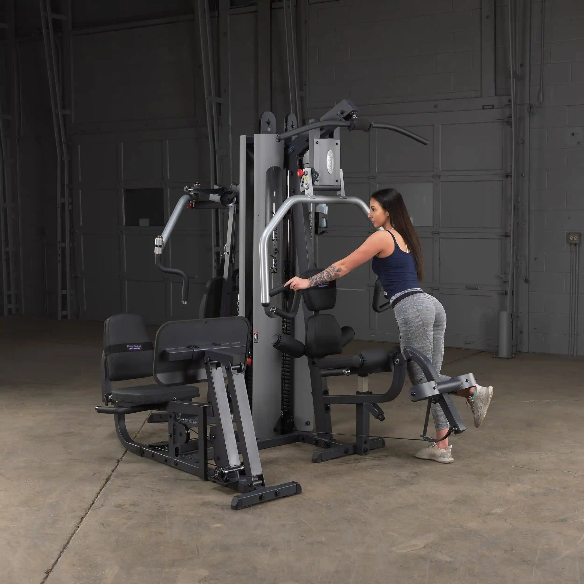 Woman using a Body-Solid home gym machine for a leg workout in a spacious industrial setting.