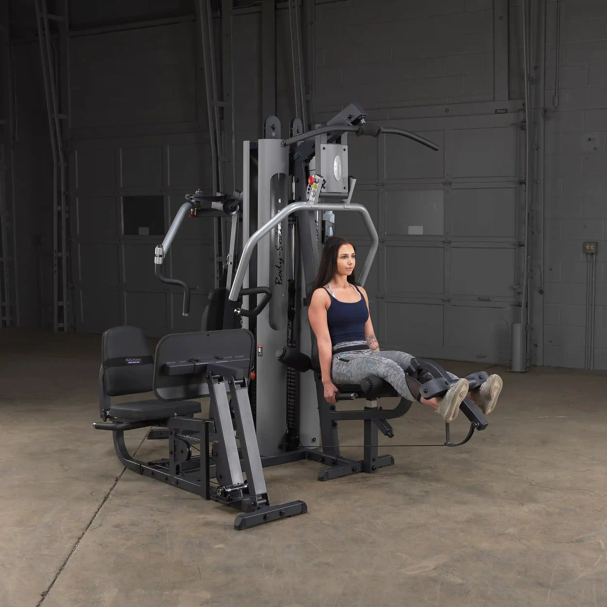 Woman using Body-Solid home gym for leg exercises in a spacious room.