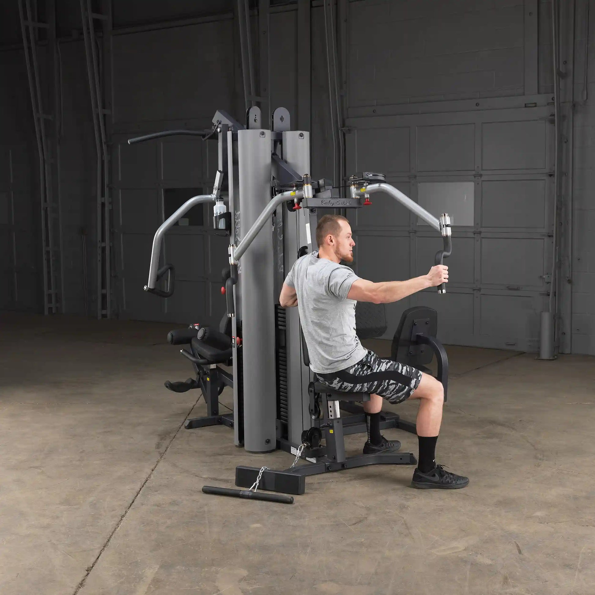 Man using Body-Solid home gym machine in a garage setting for strength training.