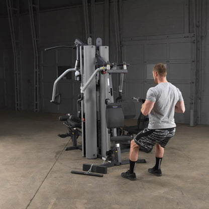 Man using Body-Solid gym machine for strength training in a garage setting.