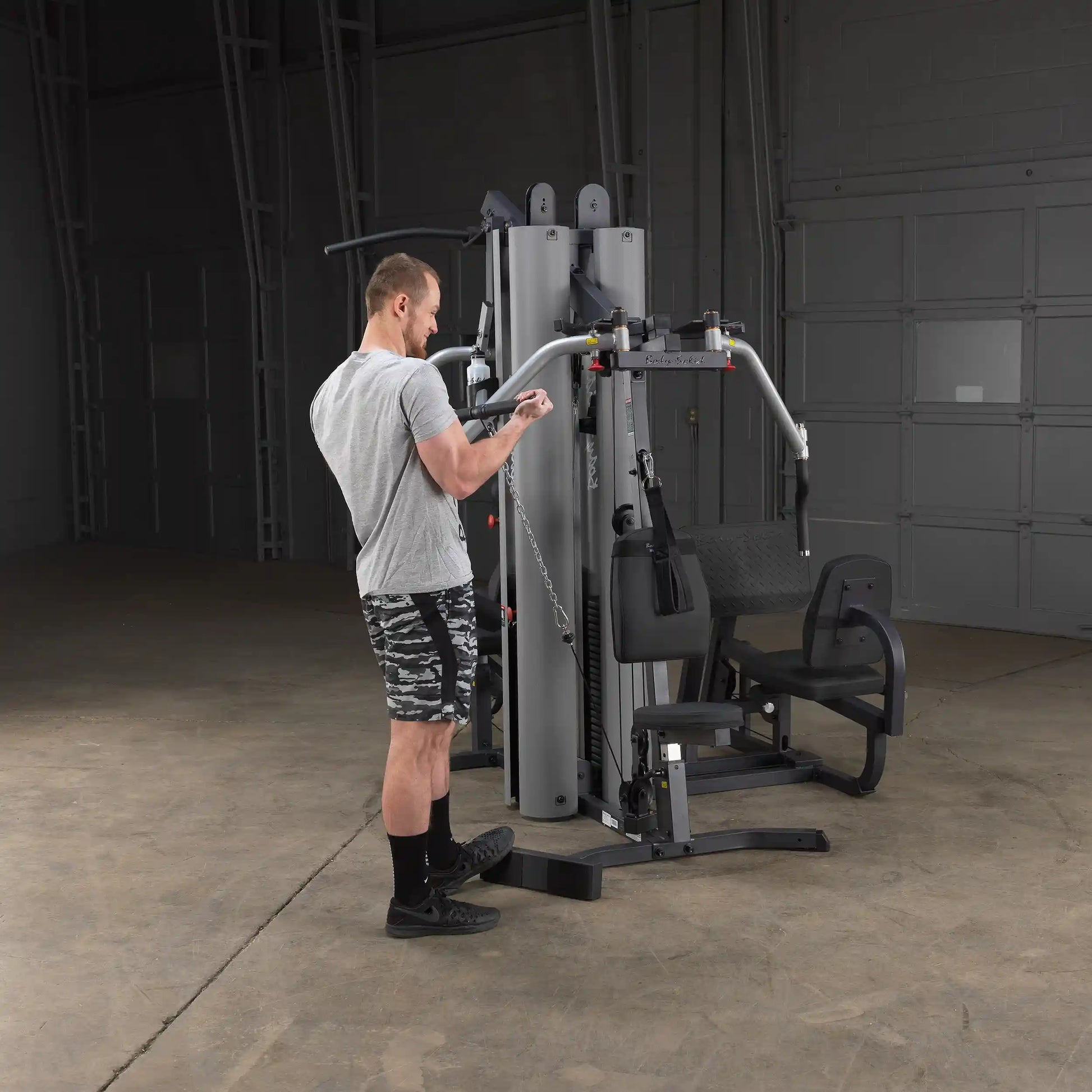 Man using a gray multi-station home gym equipment in a garage.