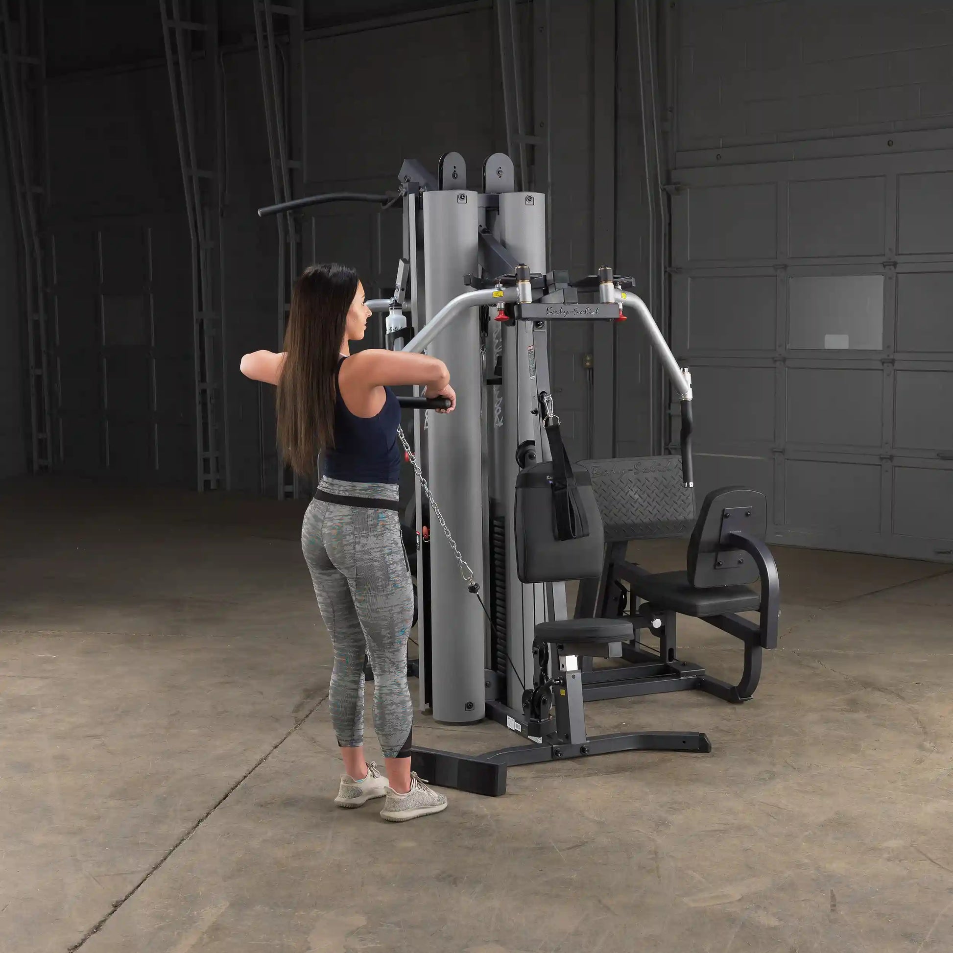 Woman using Body-Solid gym equipment for cable exercises in a spacious workout area.