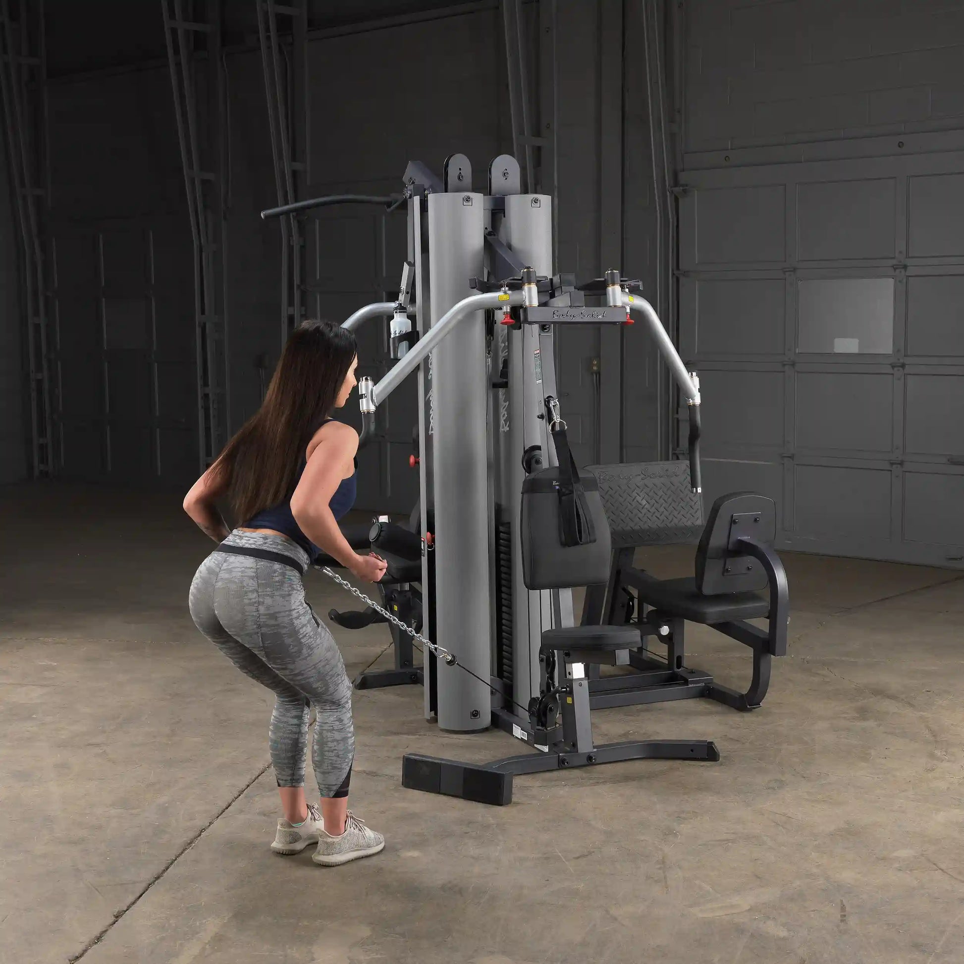 Woman using a multi-station gym machine for tricep exercise in a gray workout outfit.