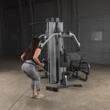 Woman using a multi-station gym machine for tricep exercise in a gray workout outfit.