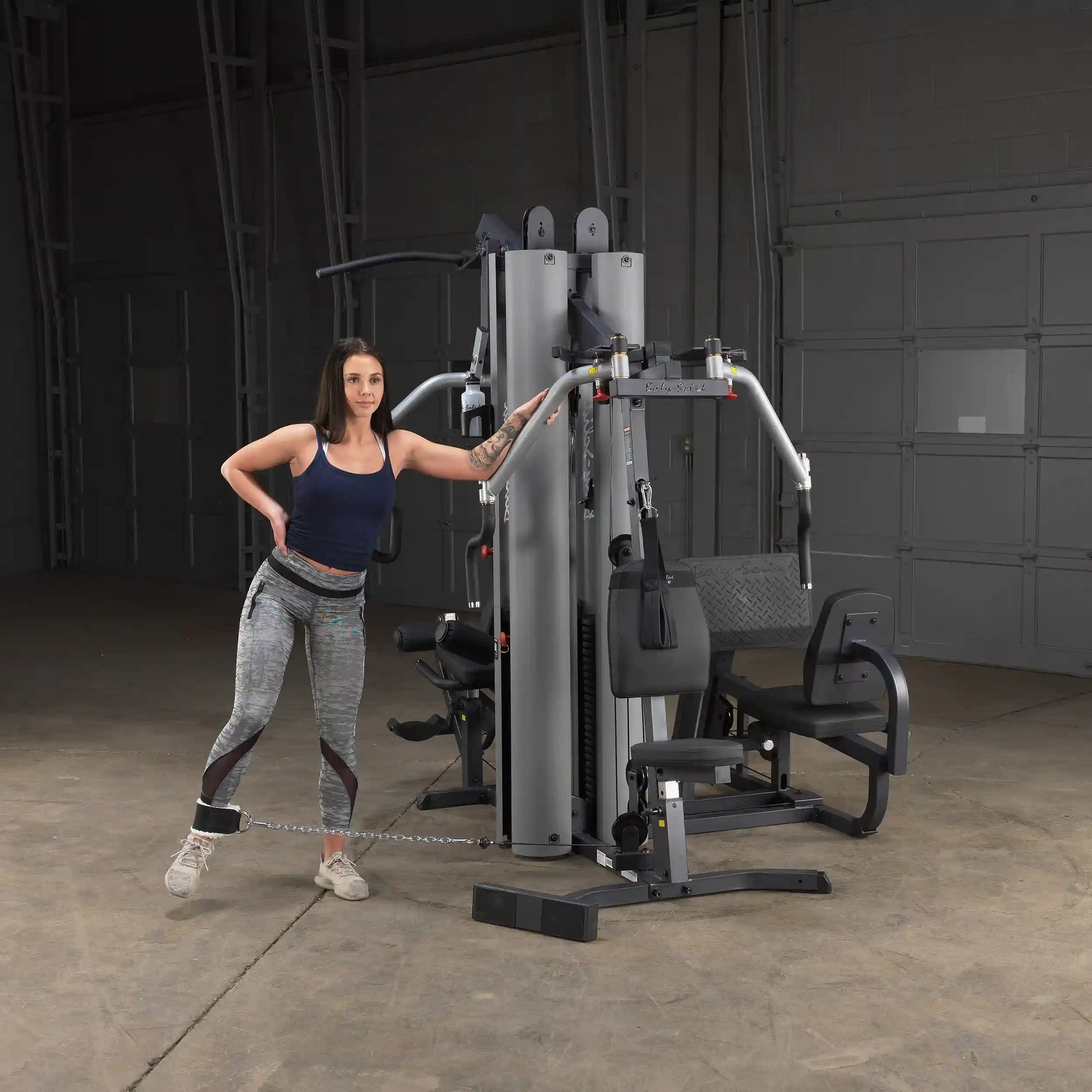 Woman using Body-Solid gym machine in gray leggings for leg workout.