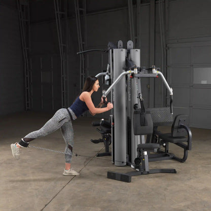 Woman using Body-Solid gym equipment for leg exercise in a dimly lit room.
