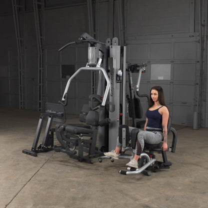Woman using Body-Solid home gym with leg extension in a spacious room.