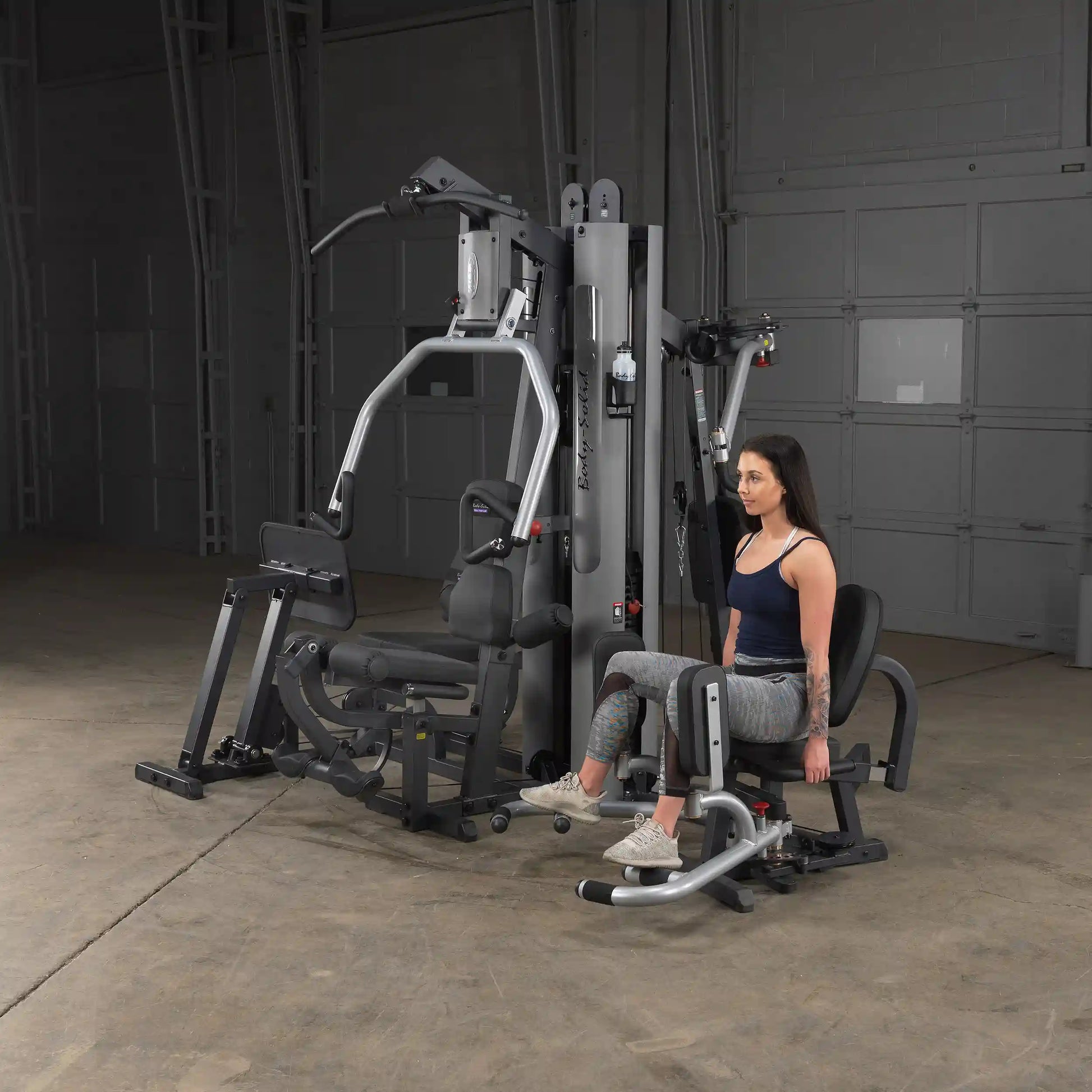 Woman using Body-Solid home gym machine with leg press in a dark room.