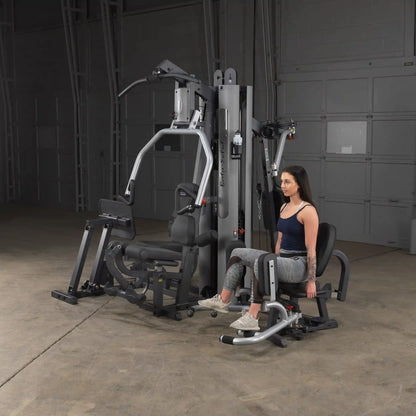 Woman using Body-Solid home gym machine with leg press in a dark room.