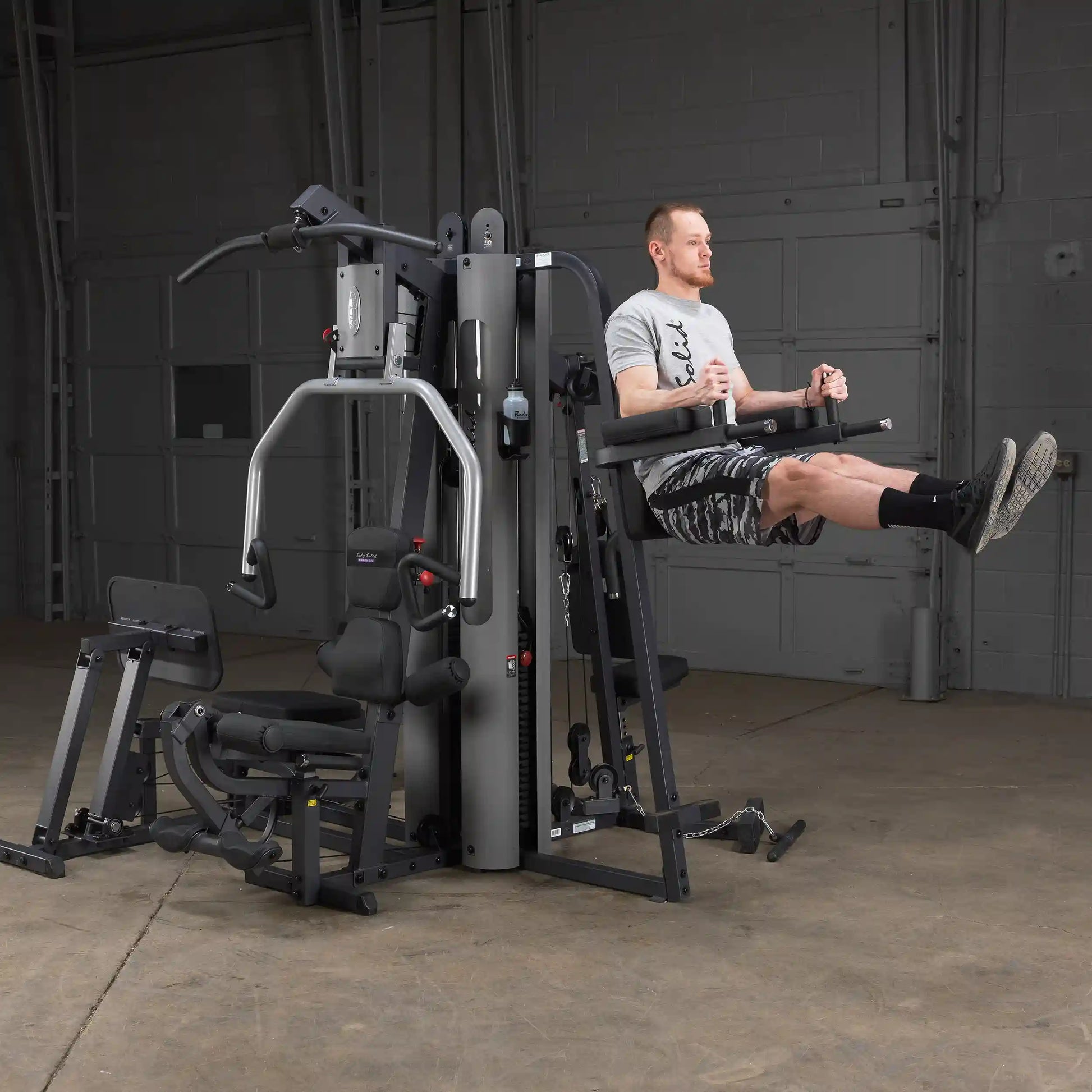 Man using Body-Solid home gym machine for leg raises in a garage setting.