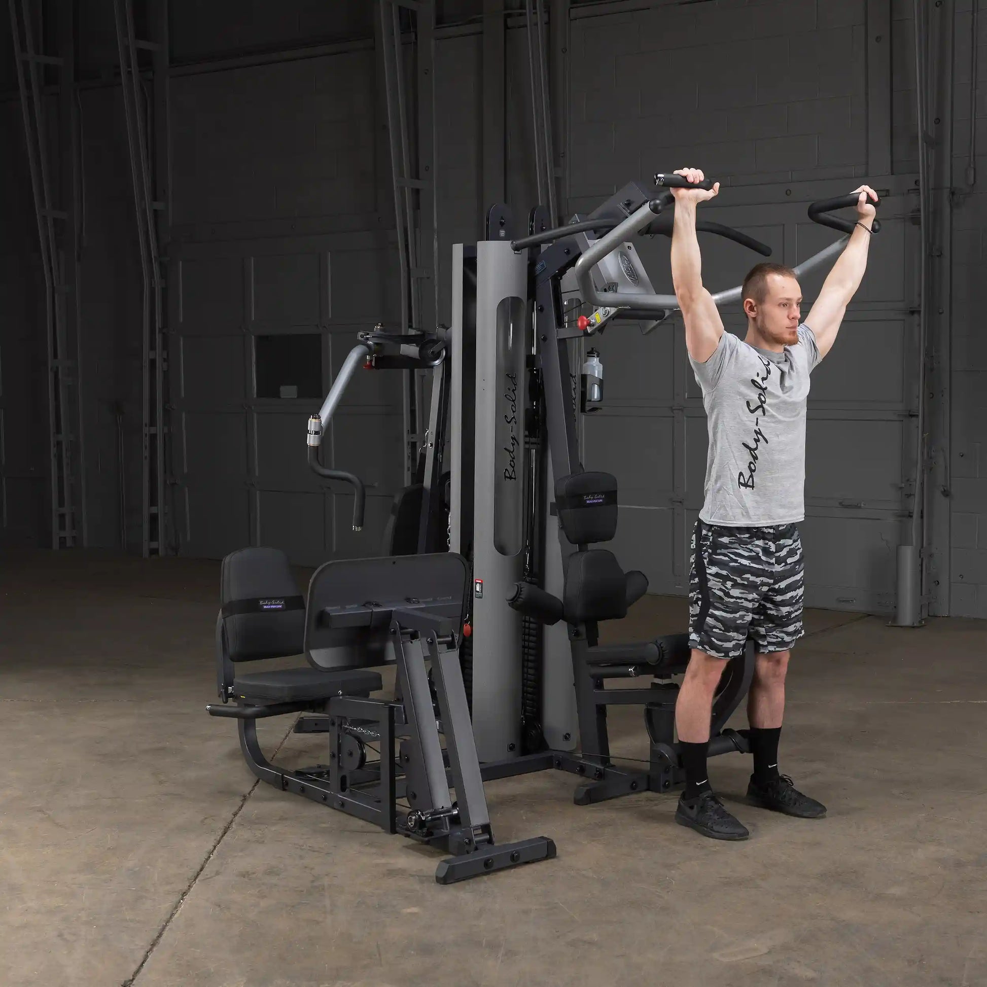 Man using Body-Solid home gym for shoulder press in a warehouse setting.