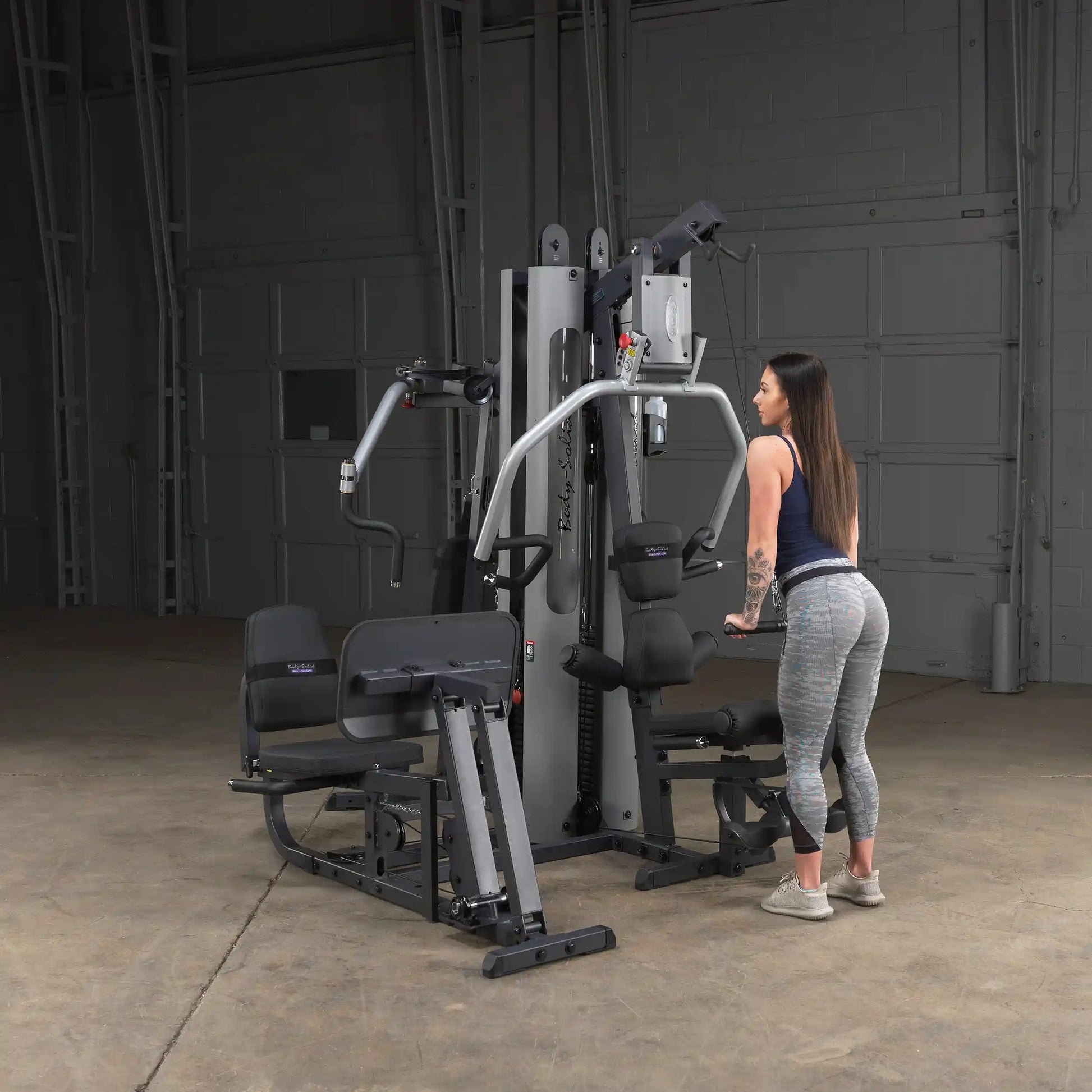 Woman using Body-Solid home gym in gray leggings, demonstrating fitness equipment features.