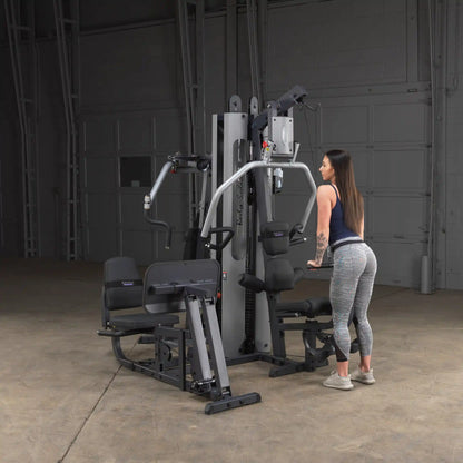 Woman using Body-Solid home gym in gray leggings, demonstrating fitness equipment features.