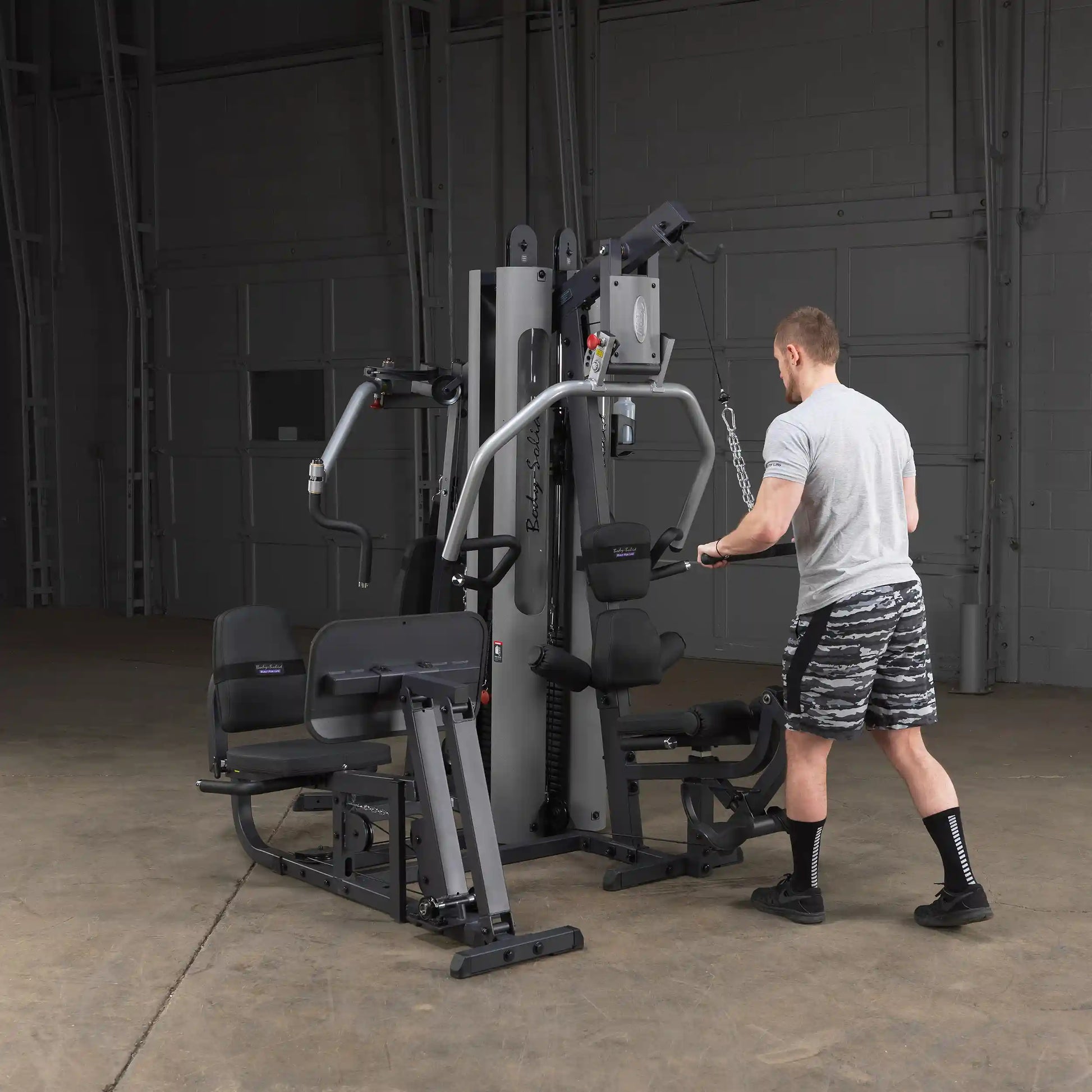 Man using Body-Solid home gym for strength training in a spacious warehouse setting.