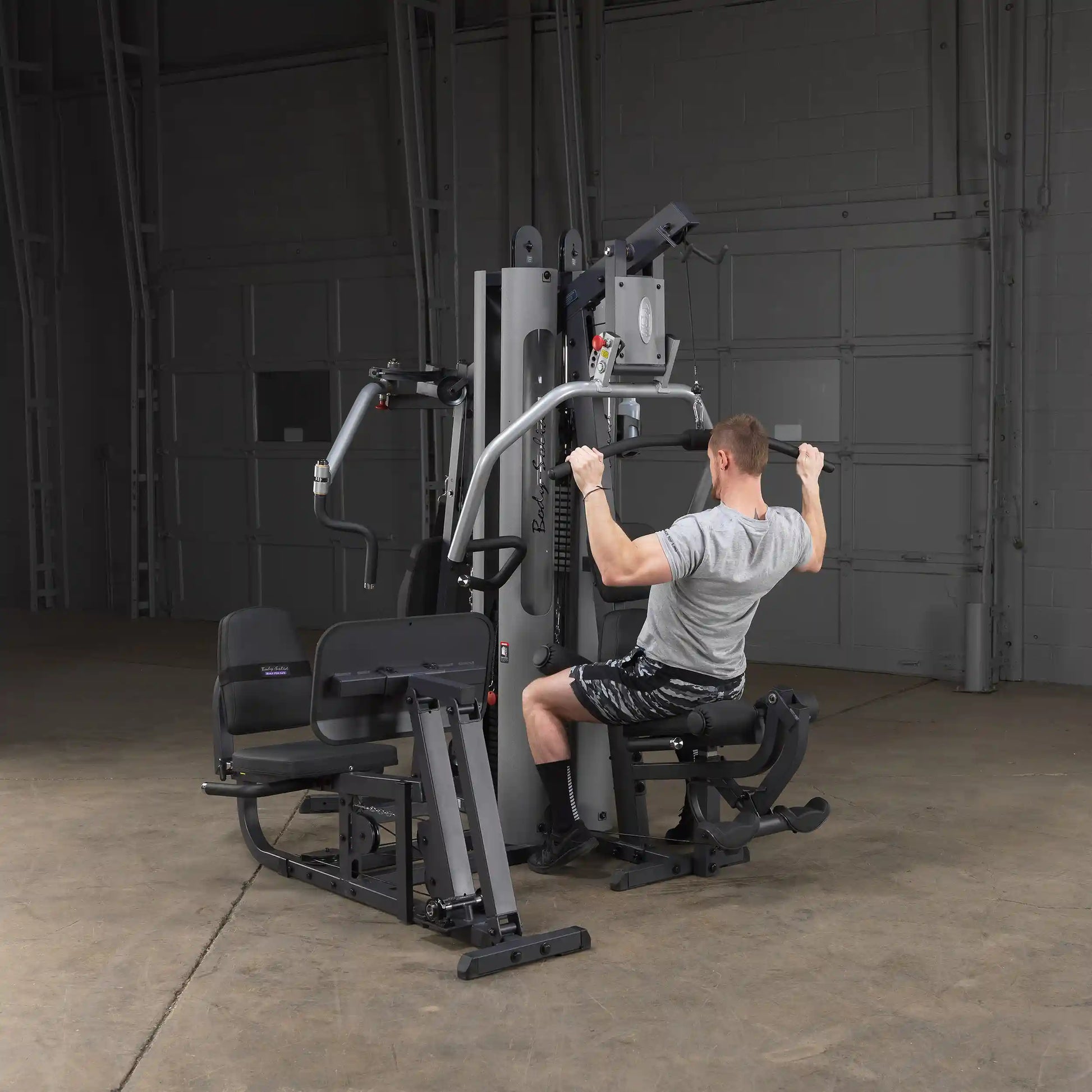 Man using a Body-Solid gym machine with lat pulldown in a spacious room.