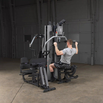 Man using a Body-Solid gym machine with lat pulldown in a spacious room.
