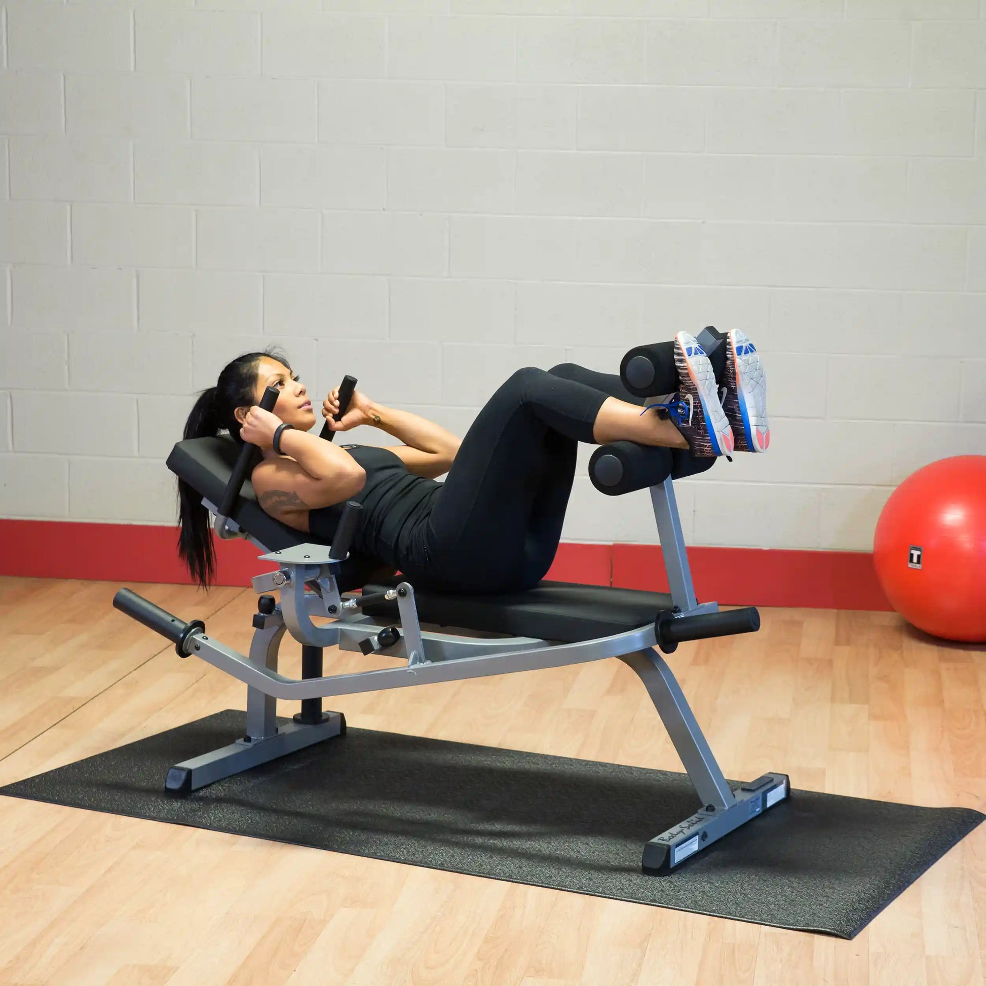 Woman using an adjustable ab bench in a gym, performing crunches in black athletic wear.