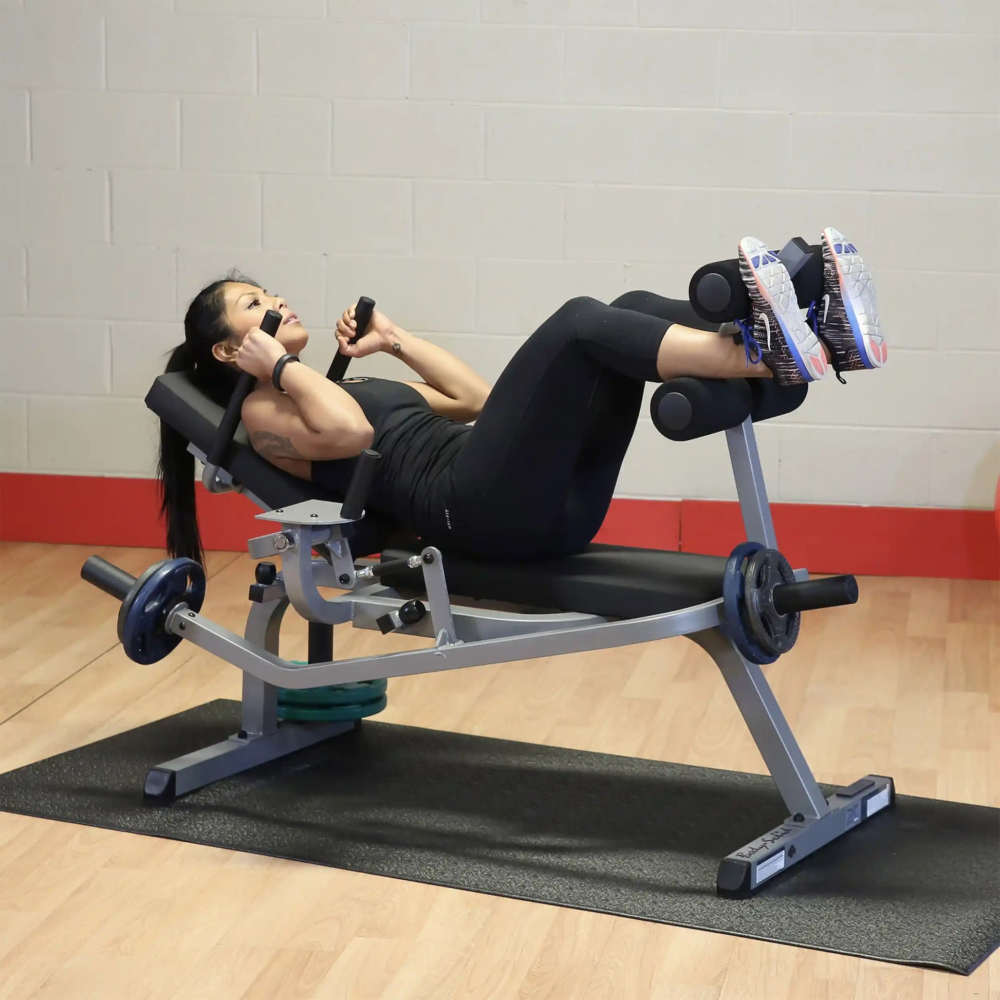 Woman using a leg press machine in a gym, wearing black workout outfit and white sneakers.
