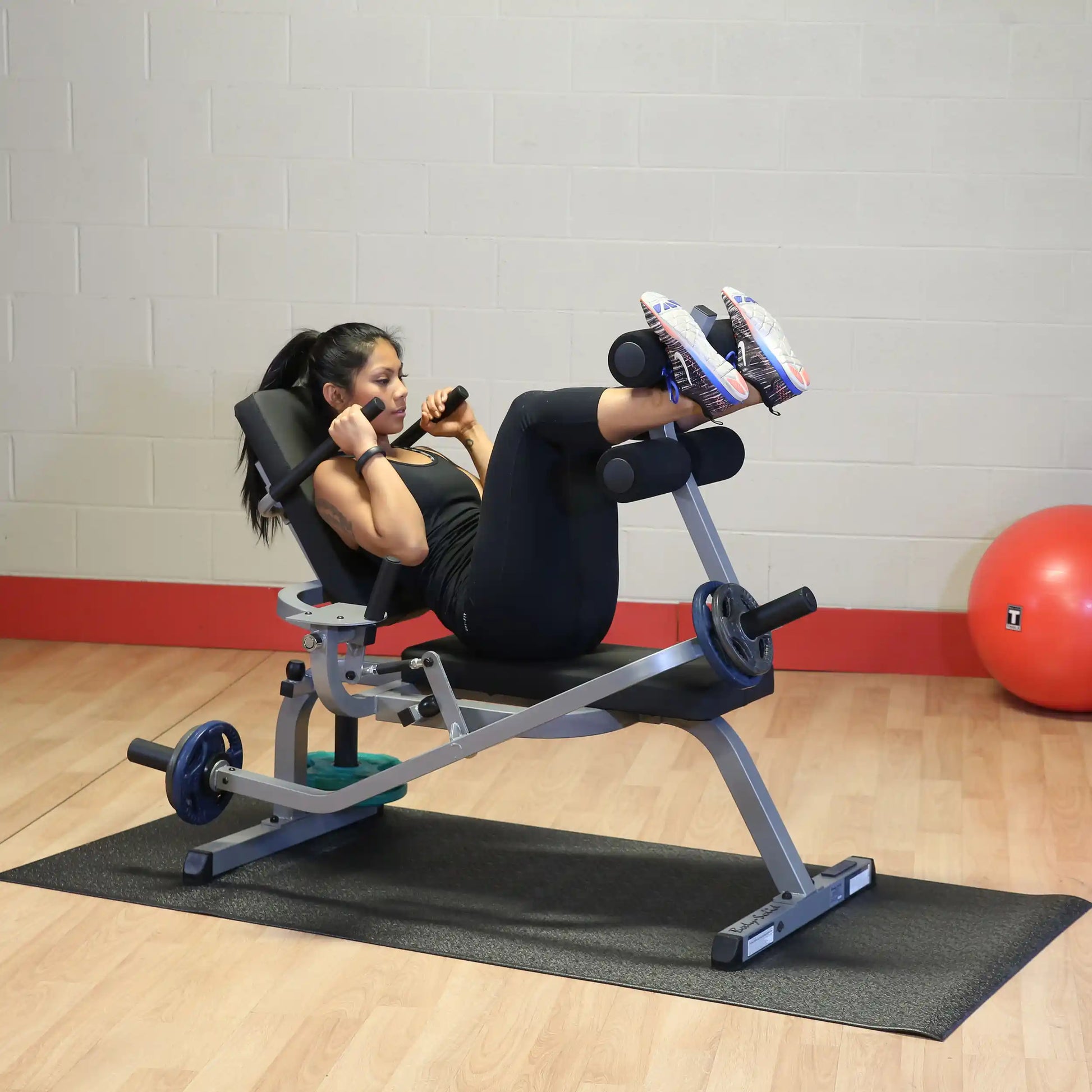 Woman using an incline bench for sit-ups, wearing black workout gear in a gym setting.