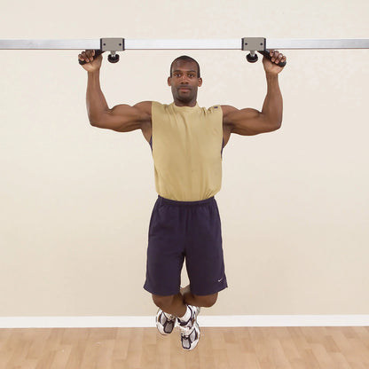 Man performing pull-up exercise on metal bar in beige tank top and navy shorts.