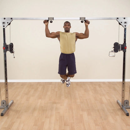 Man performing pull-up on cable crossover machine in gym.