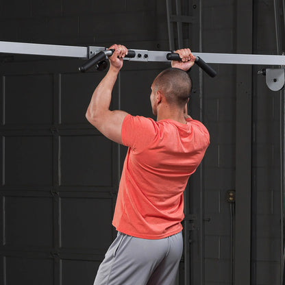 Man in orange shirt performing pull-up exercise on black pull-up bar.
