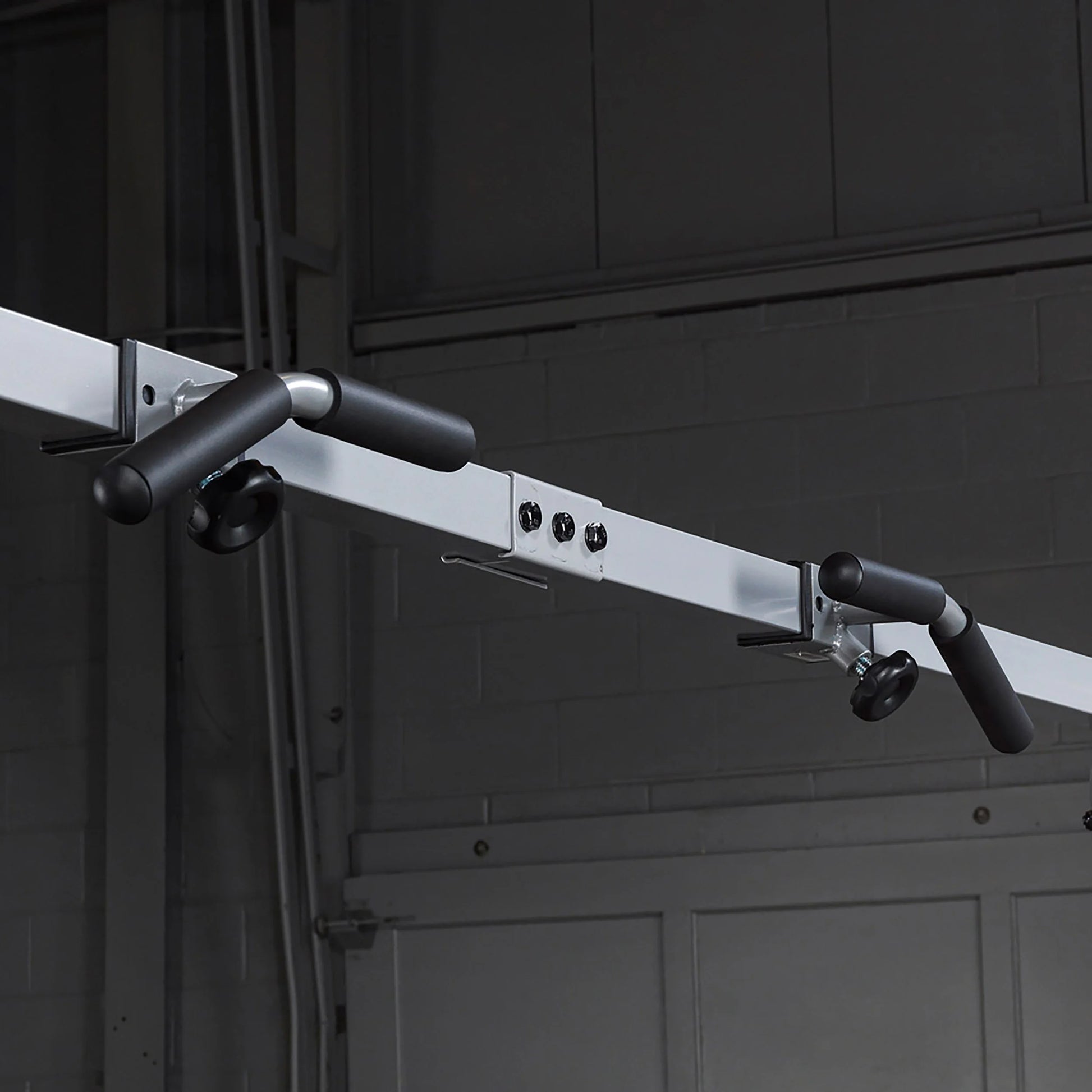 Ceiling-mounted pull-up bar with black foam grips in a gym setting.