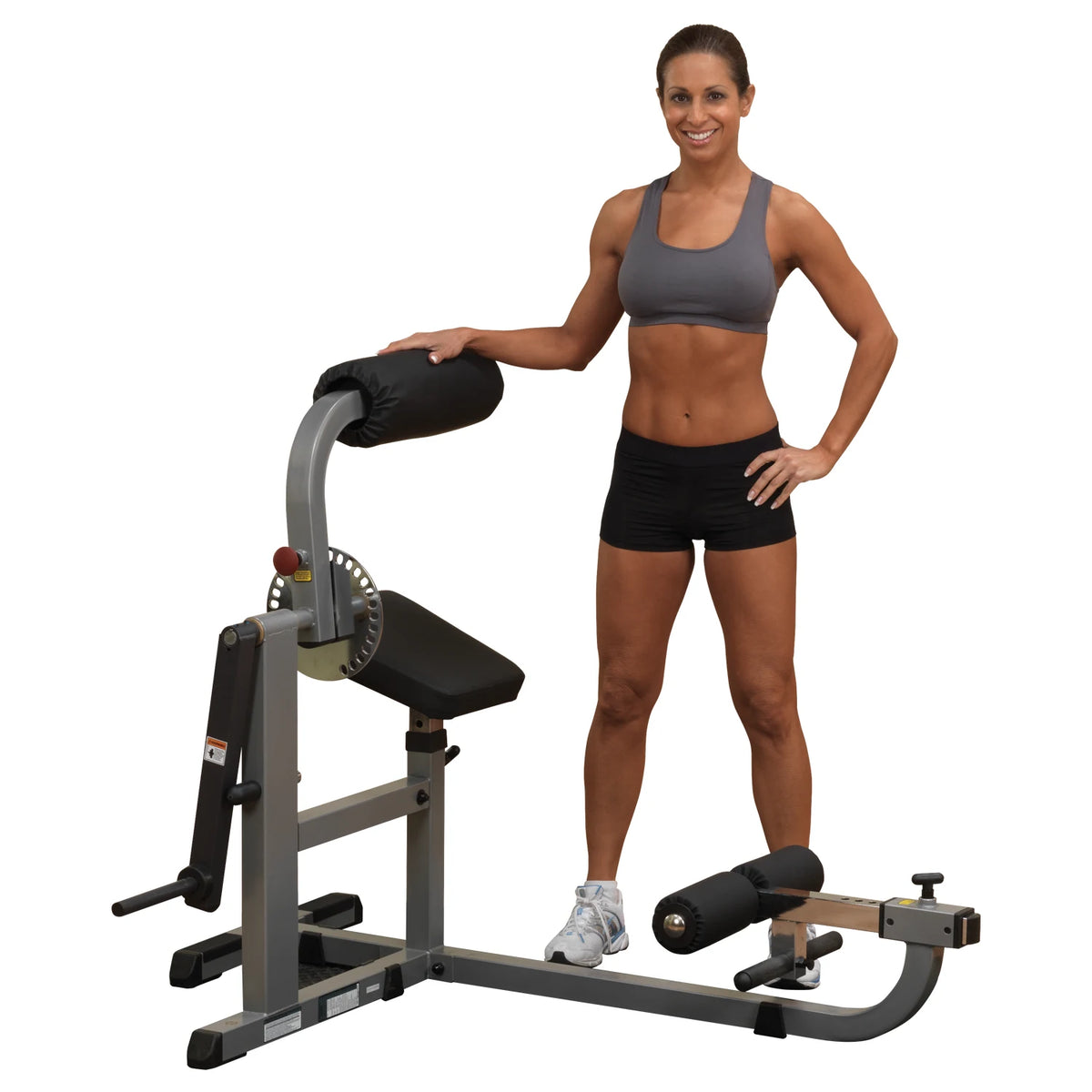 Woman standing beside Body-Solid adjustable back extension machine in gray and black workout attire.