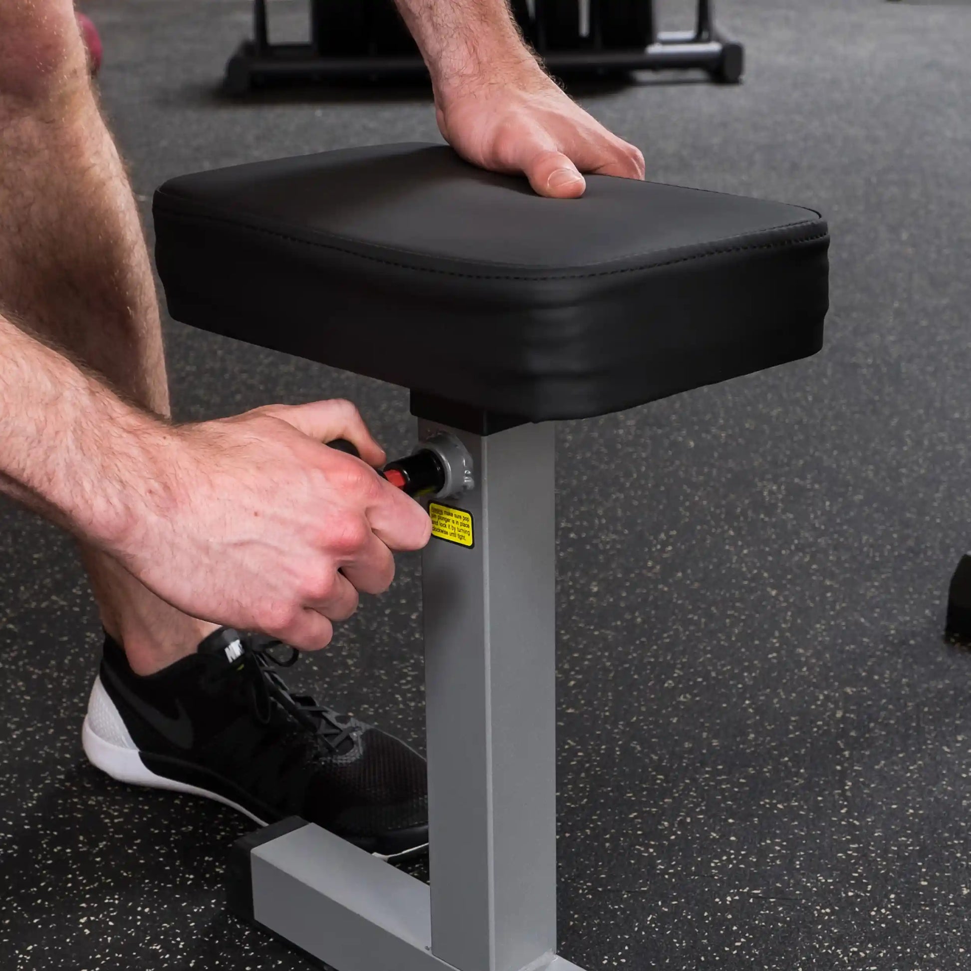 Adjustable weight bench with black cushion and silver frame being set up in a gym.