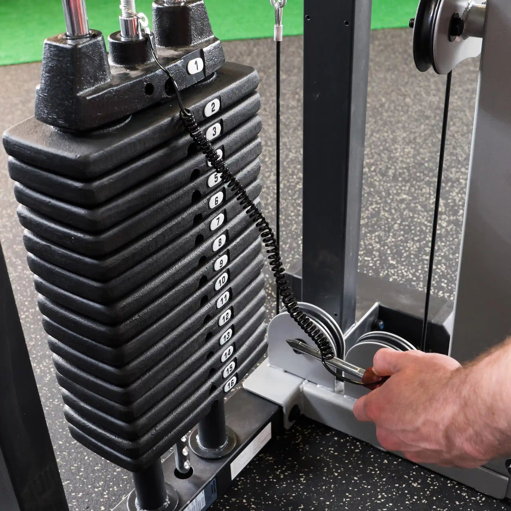 Adjusting weight stack on gym machine with numbered plates and cable.