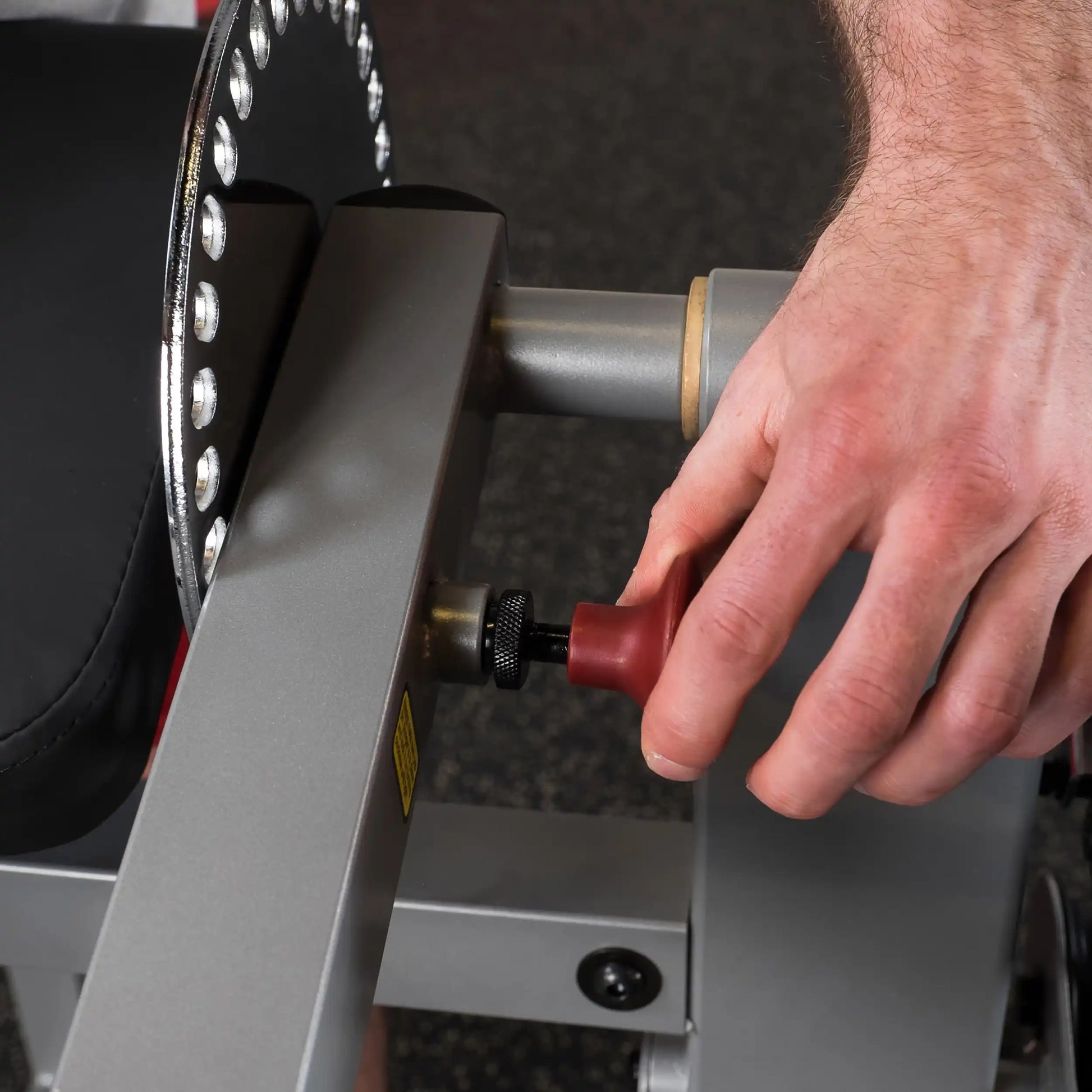 Adjusting red knob on adjustable gym bench for precise workout positioning.