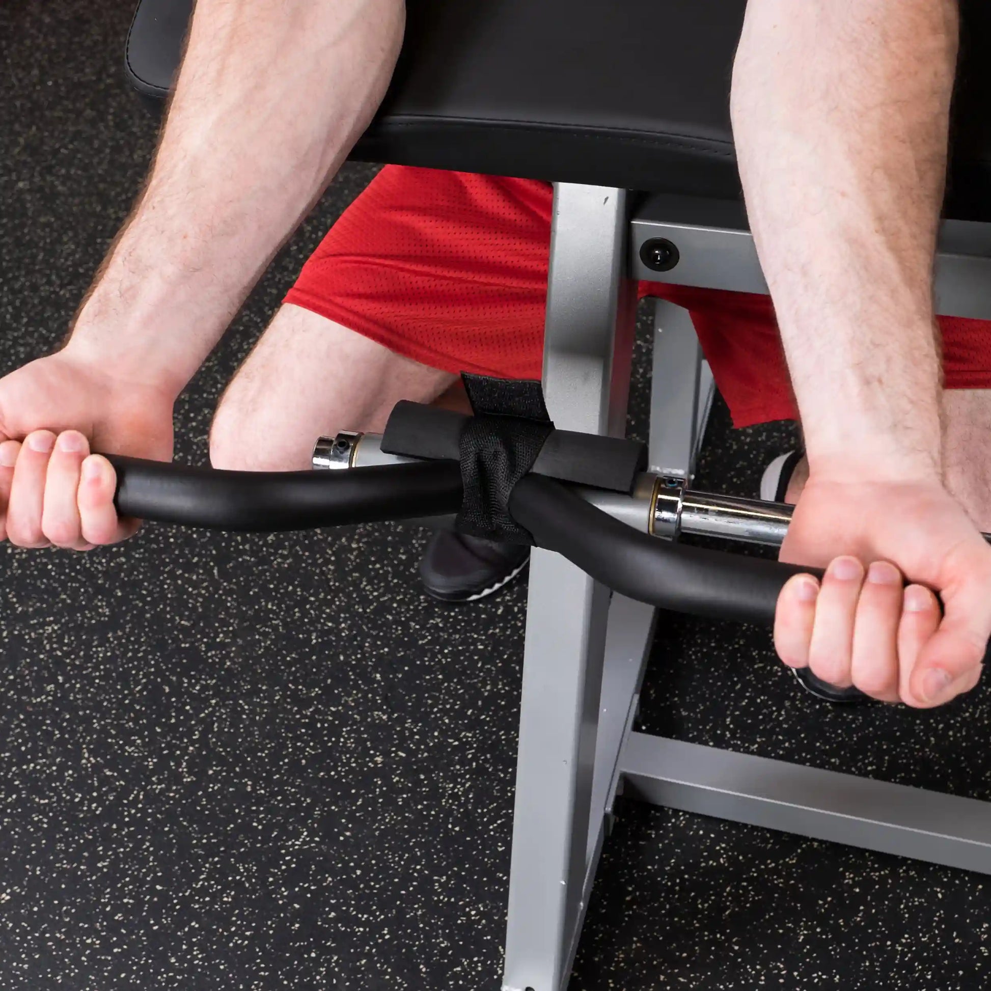 Man using a black EZ curl bar with wrist straps for bicep curls on a gym bench.