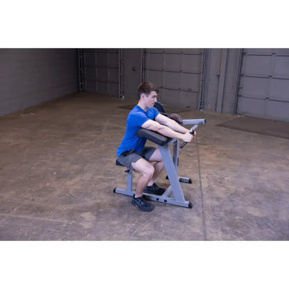 Man using seated preacher curl machine in a blue shirt and shorts for strength training.