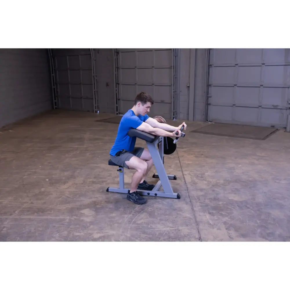 Man using a preacher curl machine in a gym wearing a blue shirt.