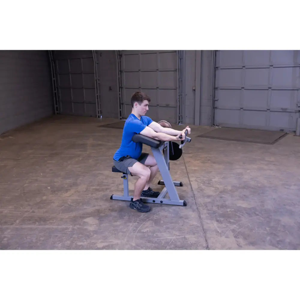 Man using preacher curl machine in blue shirt for arm workout.