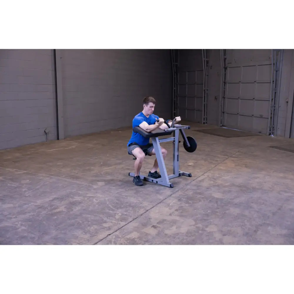 Man using a seated preacher curl machine in a spacious gym for arm workouts.