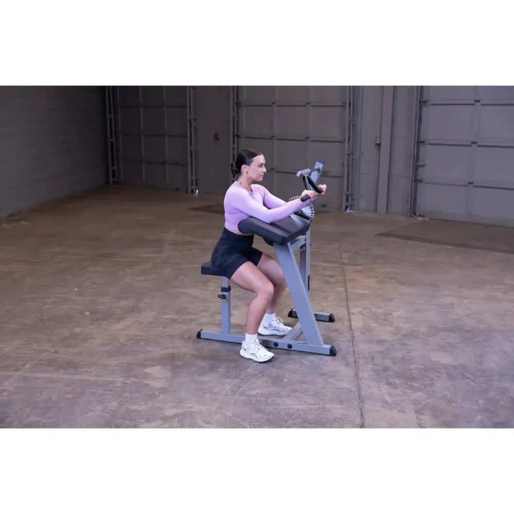Woman using a seated arm curl machine in a warehouse gym.
