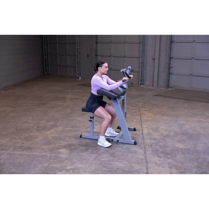 Woman using a seated arm curl machine in a warehouse gym.
