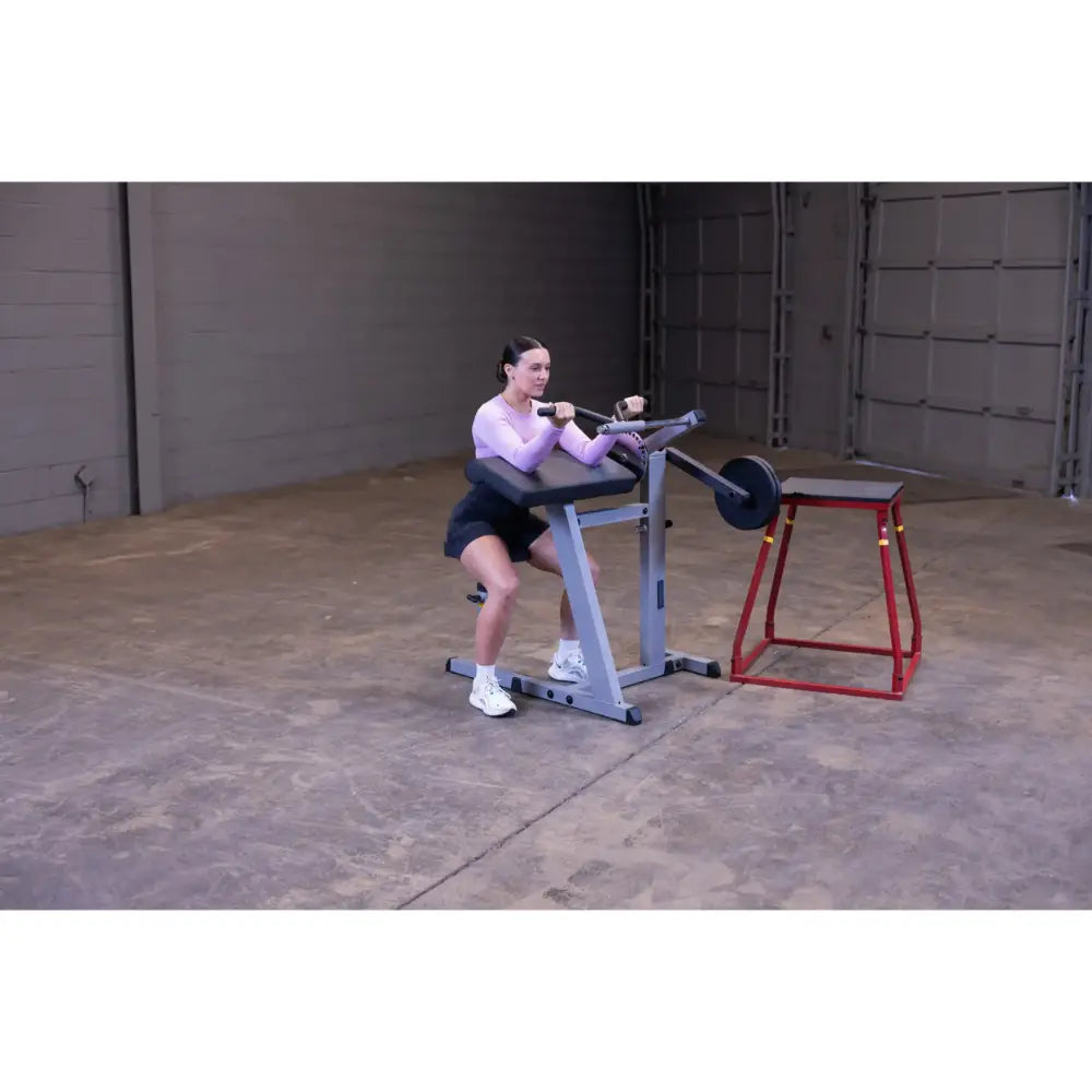 Woman using seated calf raise machine in a gym, wearing a purple top and shorts.