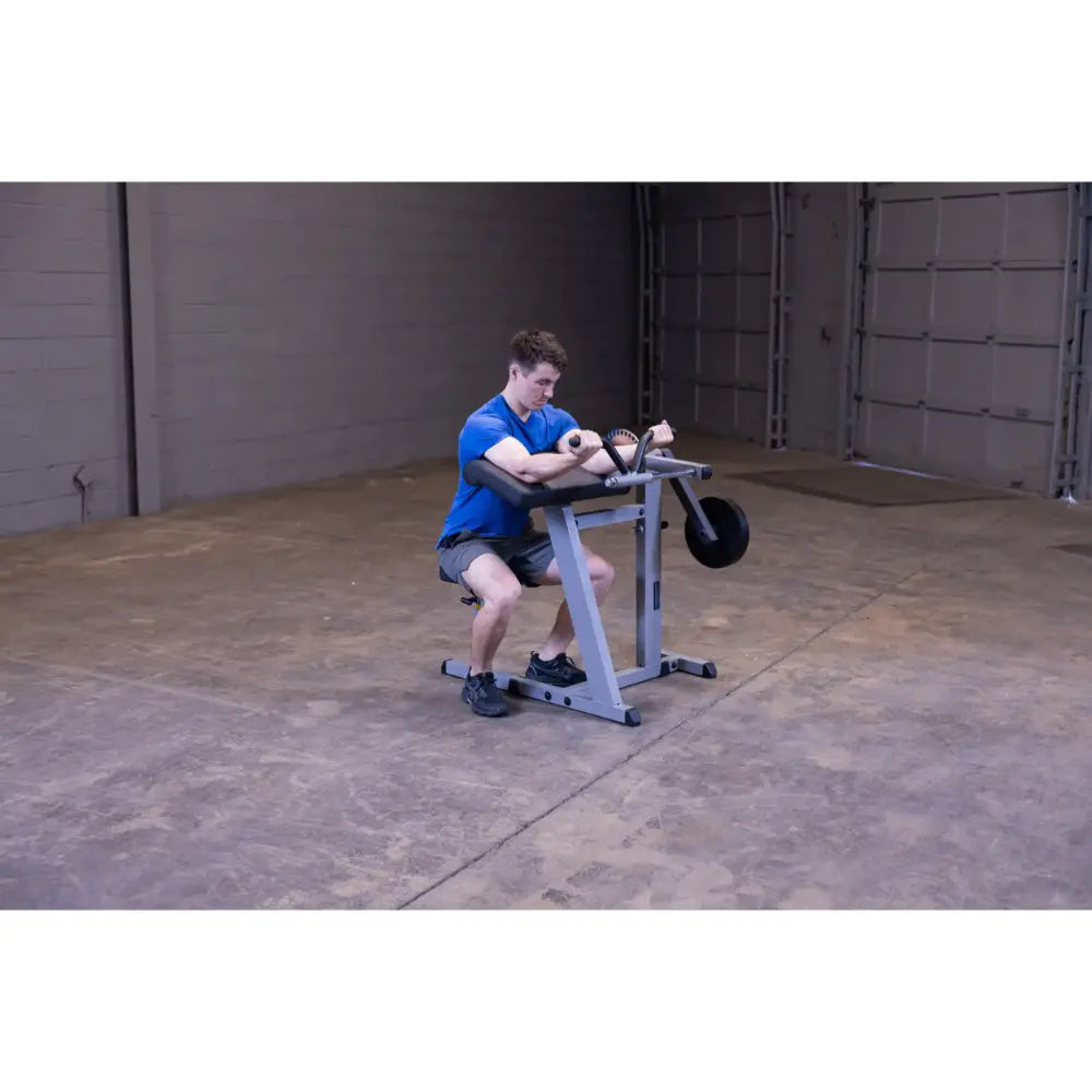 Man using a seated preacher curl machine in a gym, focusing on arm workout.