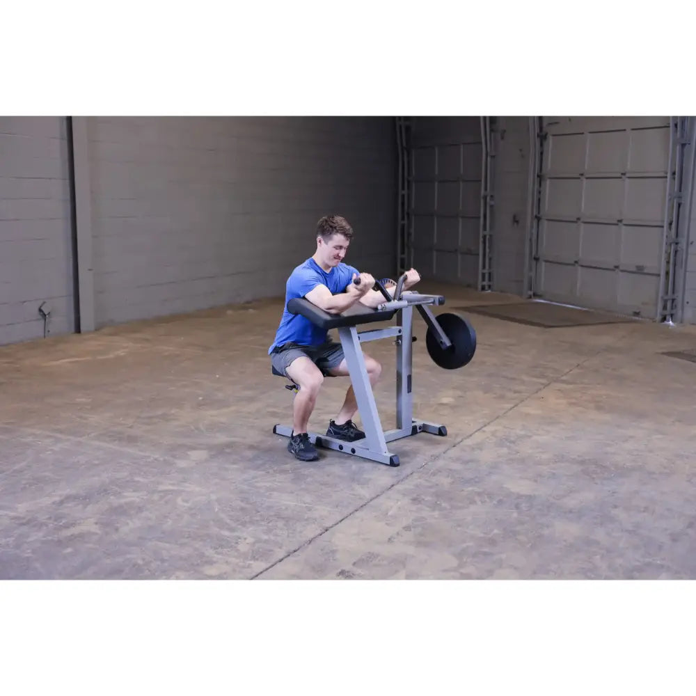 Man using a preacher curl station in a garage gym, focusing on arm workout.