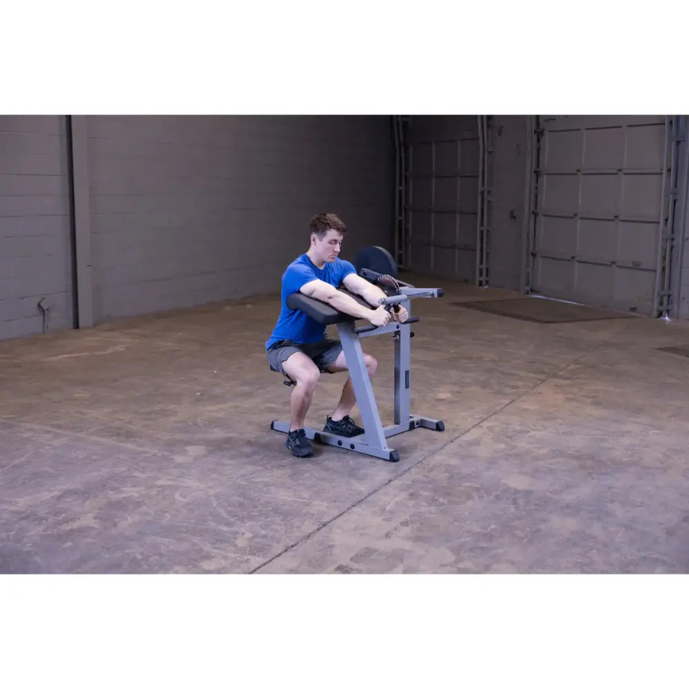 Man using a Rogue reverse hyper machine in a gym, wearing a blue shirt and black shorts.