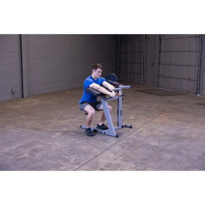 Man using a Rogue reverse hyper machine in a gym, wearing a blue shirt and black shorts.